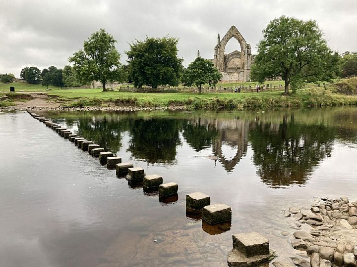 A view of Bolton Abbey ruins with the river Wharfe and stepping stones in the foreground